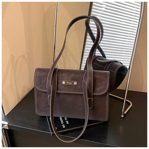 Detailed view of dark brown vintage shoulder bag with white stitching and gold logo plaque