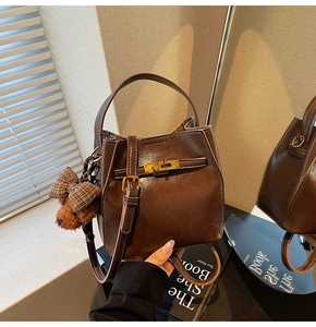 Dettaglio borsa a secchiello in pelle marrone con chiusura oro e ciondolo orsetto