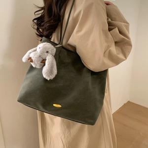 Detail of forest green suede tote bag with golden buckle and grey rabbit plush charm