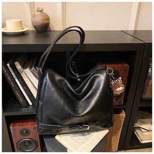Close-up of black leather hobo bag with furry monster charm and decorative bottom buckle