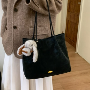 Detail of black suede tote bag with golden metal plate and plush bunny charm on shoulder