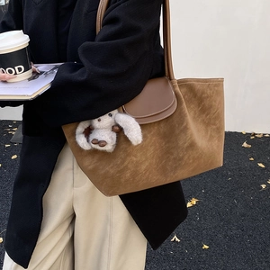 Detail of brown suede tote bag with dark leather flap and white plush bunny charm