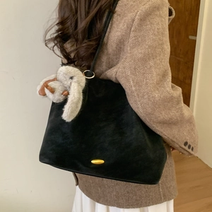 Detail of a large black suede tote bag with a golden metal buckle and plush rabbit charm