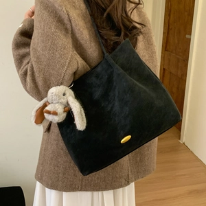 Detail of black suede tote bag with gold hardware and plush rabbit charm on model