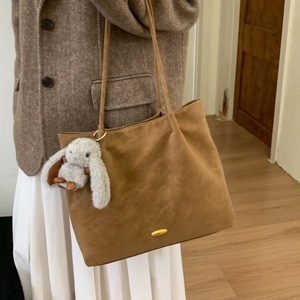 Detail view of a large brown suede tote bag with a cute white plush bunny charm