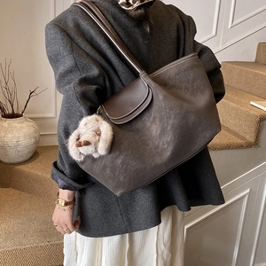 Detail of large brown tote bag with white contrast stitching and plush rabbit accessory