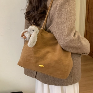 Close-up of brown suede tote bag with golden hardware and cute bunny plush pendant