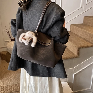 Detail of grey suede tote bag with contrast stitching and plush rabbit charm on a model