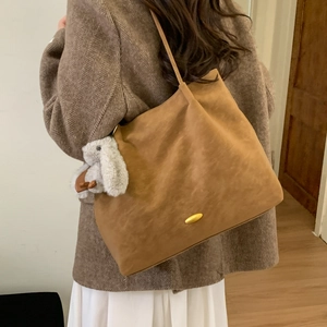 Detail of a brown tote bag featuring a golden buckle and a cute white bunny pendant
