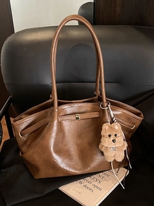 Vintage brown leather bucket tote bag with plush charm on a black leather seat