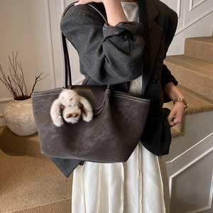 Close-up of a charcoal grey suede tote bag featuring a cute plush bunny pendant detail