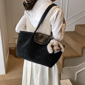 Detail of black tote bag with white stitching and grey plush bunny charm on a model