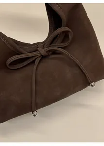 Detailed macro view of the bow-knot design and silver beads on the brown suede handbag