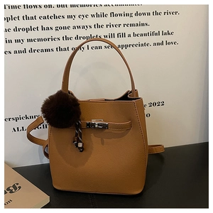 Detail van bruine emmer tas met litchi-nerf, metalen draaisluiting en bontpompon hanger