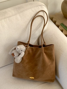 Retro brown oversized tote bag with plush rabbit charm on a minimalist cream sofa