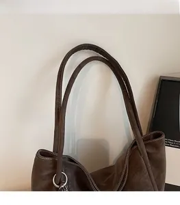 Detail of dark brown leather tote bag with white stitching, dual straps and tassel charm