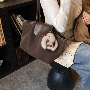 Detail of dark brown tote bag with white stitching and plush bunny charm on a model