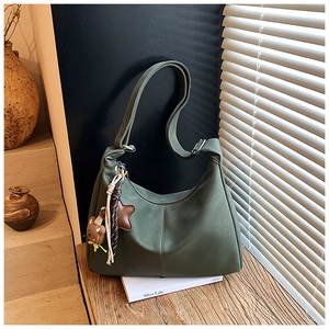 Dettaglio borsa tote verde scuro opaca con ciondolo a orsetto su tavolo in legno