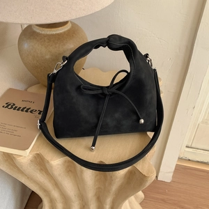 Detail of black suede handbag with knot handle and bow on a wooden display stand