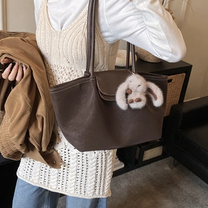 Detail of dark brown tote bag with white stitching and a plush bunny charm on shoulder