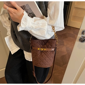 Détail d'un sac seau en daim matelassé marron avec fermoir doré et bandoulière chaîne