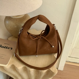 Brown leather handbag detail featuring a knot handle, bow tie, and silver metal accents