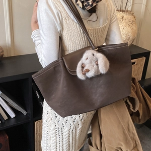 Brown leather tote bag with white stitching and a plush rabbit charm shown on shoulder
