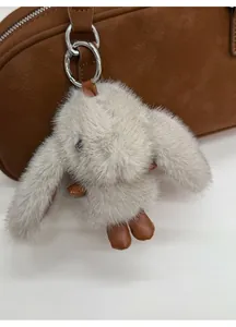 Detail of grey plush bunny charm with brown leather accents on a dark handbag
