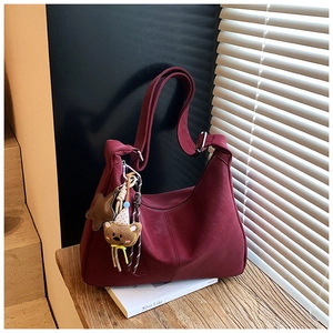 Dettaglio borsa tote bordeaux con ciondoli a stella e orsetto su panca in legno