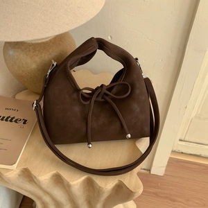 Detail of dark brown suede handbag with decorative bow on artistic wavy pedestal