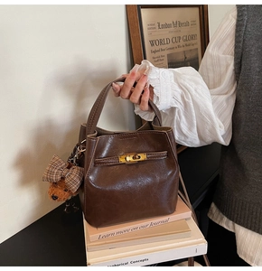 Dettaglio della borsa a secchiello in pelle marrone scuro con chiusura dorata e orsetto