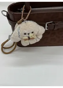 Dettaglio charm per borsa a forma di cucciolo di peluche con fiocco su borsa marrone