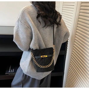 Detail of black quilted bucket bag with gold chain handle and twist-lock closure