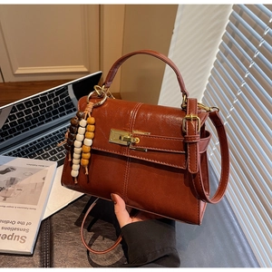 Detailed view of the dark brown glossy leather handbag with a gold-tone turn-lock and bead charm