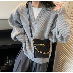 Detail of black quilted bucket bag featuring gold metal clasp and chain strap