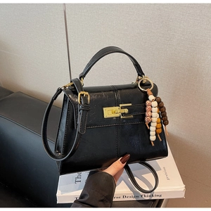 Detail of black glossy PU leather handbag with gold clasp and retro beaded charm on book