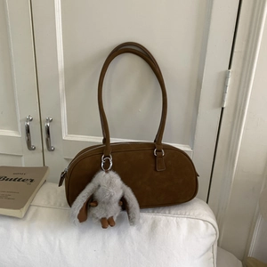 Brown suede Boston bag with a cute long-eared bunny plush charm on a cozy sofa