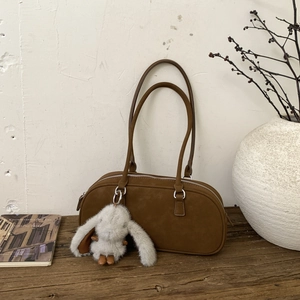 Detailed view of a brown suede bowling bag with a cute plush rabbit charm on a wooden table