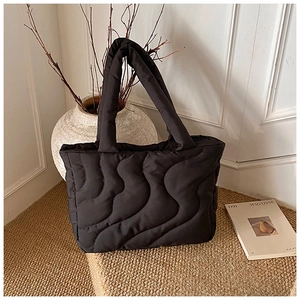 Detail of wave quilted black puffer tote bag on textured surface in a lifestyle setting