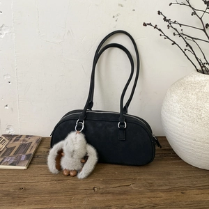 Minimalist black suede Boston bag with plush rabbit charm on vintage wood surface