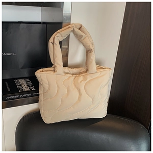 Detail of beige quilted puffer handbag with soft wavy stitching and padded handle texture