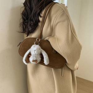 Dark brown suede shoulder bag with a white rabbit charm worn over a beige wool coat