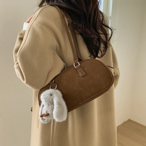 Close-up of brown suede shoulder bag with thin straps and a white plush bunny charm