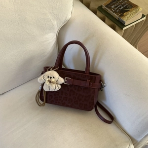 Dettaglio borsa a tracolla in pelle bordeaux con stampa leopardata e ciondolo a cucciolo