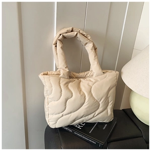 Detail of beige quilted puffer tote bag with wavy stitching on a lifestyle background