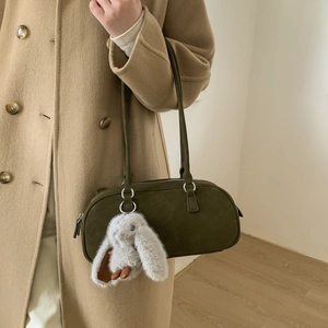 Olive green suede Boston bag with plush rabbit charm worn by a model on the shoulder