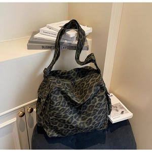 Close-up of leopard print canvas bag with adjustable strap and zip closure on a soft stool