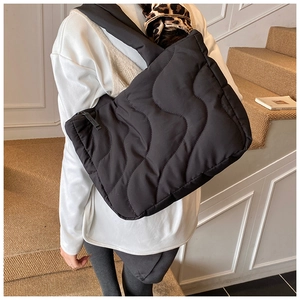 Detail of black quilted puffer tote bag with wave-pattern stitching and wide shoulder strap