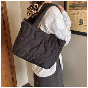 Detail of black quilted shoulder bag featuring wavy stitching and glossy nylon texture