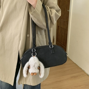 Detail of black suede shoulder bag with a cute white bunny plush keychain charm